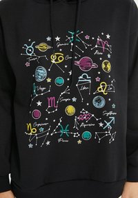 Sweat à capuche noir arborant un design astrologique coloré avec des planètes, des étoiles et des symboles du zodiaque. Imprimé en plusieurs couleurs vives sur le devant.