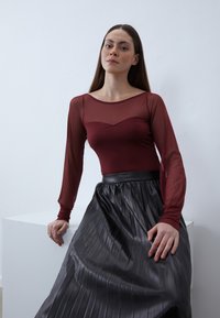 Burgundi hosszú ujjú felső átlátszó dizájnnal �és szív alakú dekoltázzsal, fekete plisszírozott szoknyával kombinálva, amely sima textúrájú.