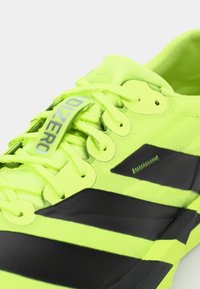 Neon yellow athletic shoe with black stripes, featuring a textured upper, round laces, and a branded pull tab.