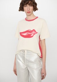 Cream t-shirt with red lips graphic, short sleeves, and a pink collar; paired with shiny silver pants featuring a front button closure.
