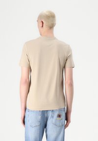 Beige bomull t-skjorte med korte ermer og rund hals, parret med lyseblå denimjeans med broderte logodetaljer på baklommen.