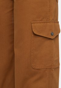 Brown cargo pants with a distressed texture. Features a side pocket with a flap and black snap button, stitched seams, and a straight cut.