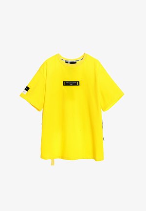 Camiseta de algodón amarilla con cuello redondo, mangas cortas y una etiqueta rectangular negra en el pecho con detalles en texto.