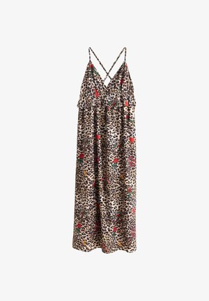 Frau trägt ein Leopardenmuster-Kleid mit roten Blumenakzenten, schwarze Lederjacke, die von einer Schulter rutscht, geschichtete Halsketten und beige Stiefeletten.