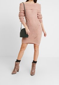 Strickkleid mit Carmenausschnitt in zartem Rosa, mit figurbetontem Schnitt und strukturierten Streifen. Kombiniert mit Schlangenleder-Stiefeletten und einer kleinen dunklen Handtasche.
