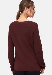 Burgundy knitted sweater with a ribbed texture, round neckline, and raglan sleeves, featuring a relaxed fit and subtle stitching details.