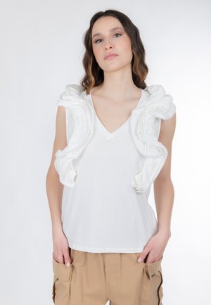 Hvid ærmeløs top med V-hals, der har teksturerede flæsedetaljer langs skuldrene. Blødt stof og afslappet pasform.