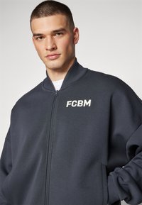 Marineblouson mit Reißverschluss und geripptem Kragen, mit auf gesticktem weißen "FCBM"-Logo auf der Brust. Hergestellt aus weichem, strukturiertem Stoff.