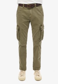Pantalones cargo verde oliva con bolsillos laterales, cremallera y presillas para cinturón, fabricados en suave tejido de algodón, combinados con zapatillas beige claras.