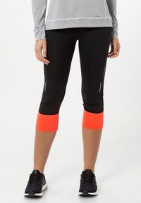 Leggings capri negros con puños en neón naranja contrastante, que cuentan con acentos reflectantes y un diseño ajustado para uso atlético.