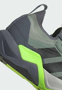 Chaussure de sport avec une tige grise texturée et des accents verts, une forme en couches et un détail TORSION SYSTEM prononcé sur la semelle.