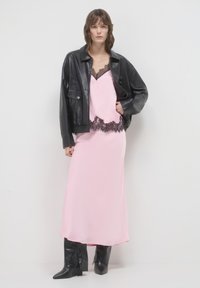 Robe en satin rose avec des bordures en dentelle, superposée sous une veste en cuir noire cropped. Des bottes noires montantes complètent l'ensemble.