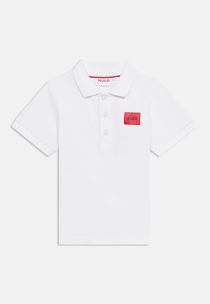 Biała koszulka polo z krótkim rękawem, trzema guzikami z przodu i czerwonym prostokątnym naszywką z napisem "HUGO" na lewej piersi.