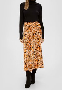 Fållad kjol i orange, svart och krämfärgad blommönster; bärs med en svart polotröja. Har ett elastiskt midjeband och strukturerad tyg.