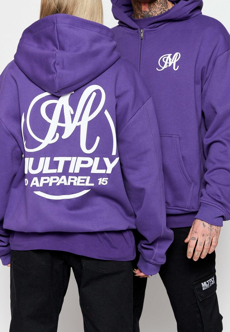 Lila Kapuzenpullover mit großem weißen Drucklogo auf dem Rücken, das ein stilisiertes 'M' und "MULTIPLY APPAREL 15" zeigt, aus weichem Stoff, lässiger Schnitt.