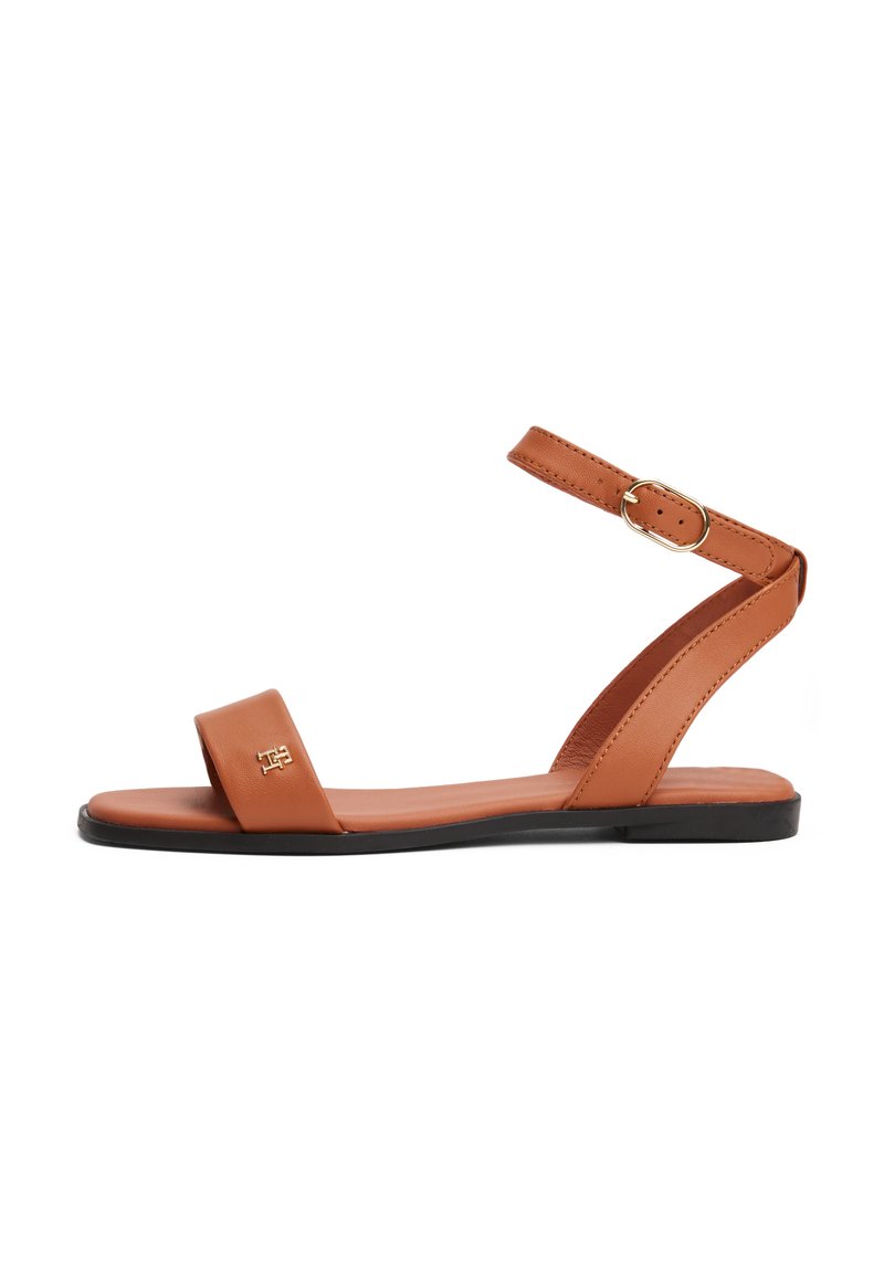 Brune lædersandal med en bred tårem, en tynd ankelrem med spænde og en flad sål. Minimalistisk design med stikninger.