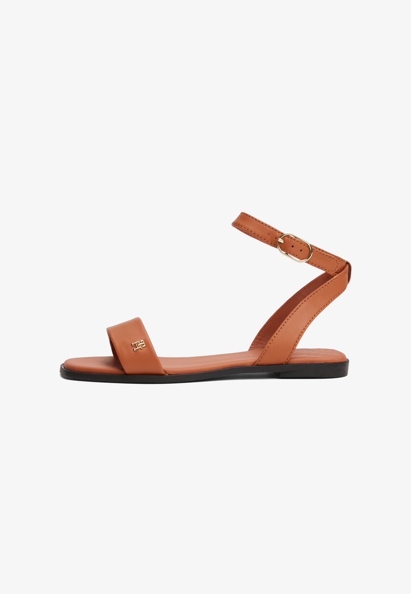Sandale din piele maro, cu un bretele lat pe degete, un bretele subțire pentru glezna cu cataramă și o talpă plată. Design minimalist cu accente cusute.