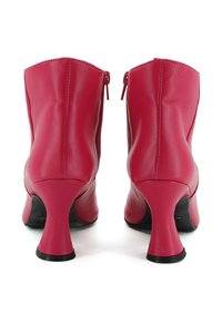 Stivaletti alla caviglia in pelle rossa con tacco curvo, chiusura con zip sul retro, texture liscia e punta arrotondata.