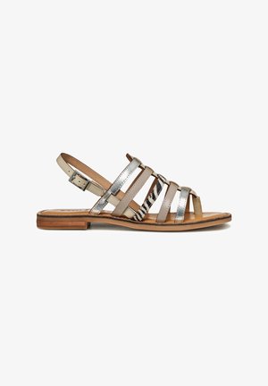 Sandalia plana con tiras en beige, plateado y estampado de cebra, con hebilla ajustable en el tobillo y suela marrón claro con tacón bajo.