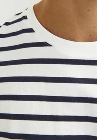 Hvid bomulds t-shirt med vandrette marineblå striber, en klassisk rund halsudskæring og synlige sting langs kraven og skuldrene.