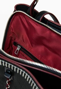 Schwarze Ledertasche mit burgunderrotem Satinfutter im Innenraum, ausgestattet mit einer Reißverschlusstasche und silberner Reißverschlussbeschlägen. Gestickte Akzentdetails sichtbar.