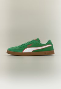 Πράσινο αθλητικό παπούτσι Puma με λευκή και κόκκινη ρίγα, καφέ σόλα και λογότυπο Puma στο πλάι και στη σόλα, απεικονίζεται σε προφίλ σε ουδέτερο φόντο.