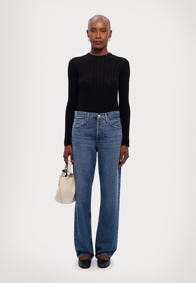 Zwarte geribbelde langemouwen top, lichtblauwe wijde jeans, kleine off-white handtas en zwarte flats. Focus op textuur en pasvorm.