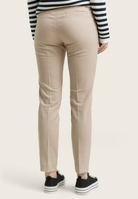 Beige střižené kalhoty s úzkým střihem, se zadními kapsami a hladkým povrchem, doplněné černobílými pruhovanými slip-on botami.