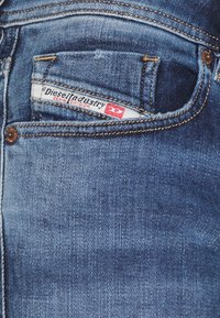 Blue denim jeans with a textured finish. The front pocket features a label reading "Diesel Industry Denim Division" in white and red.