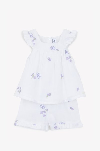 Hvit bomulls todelt antrekk med broderte lilla blomster. Toppen har volangermarmer; shortsen har en flosset kant. Lett tekstur.