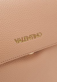Sac en cuir texturé rose avec un logo "Valentino" doré et un design épuré. La fermeture est un bouton-pression discret avec une finition soignée.