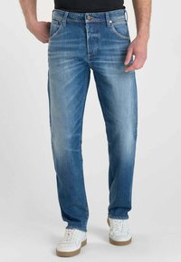 Jeans in denim blu con vestibilità dritta, leggera scoloritura, cinque tasche e dettagli in metallo. Indossati con sneakers bianche.