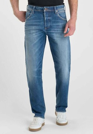 Blauwe spijkerbroek met een rechte pasvorm, lichte vervaging, vijf zakken en metalen hardwaredetails. Gemaakt met witte sneakers.