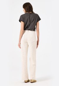 Grijze shirt met korte mouwen en opgerolde mouwen, gecombineerd met lichtbeige, gestructureerde, high-waisted broek met twee achterzakken. Casual schoenen.