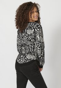 Sweter w czarno-białe wzory z mieszanką abstrakcyjnych grafik. Dzianinowa tekstura; długie rękawy i kontrastowy ściągacz u dołu. Noszony z czarnymi dżinsami.