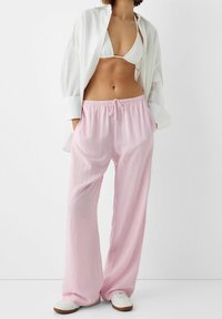 Light pink striped pajama pants with an elastic waistband and drawstring, paired with a white oversized shirt and white slip-on shoes.