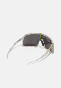 Gafas de sol con montura transparente que presenta un patrón moteado en tonos de amarillo y naranja. Lentes oscuros y varillas rectas con detalles de marca.