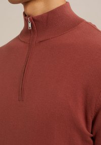 Pulover cu fermoar pe jumătate în culoare bogată de burgund, cu un guler ribflat și un material tricotat fin pentru căldură și confort.