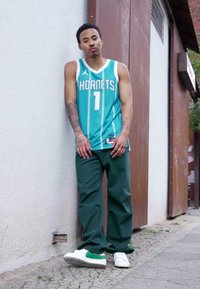 Teal basketballtrøje med "HORNETS" i hvide bogstaver, parret med mørkegrønne bukser og hvide sneakers med grønne accenter.