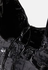 Μαύρη τσάντα tote από γυαλιστερό, υφασμάτινο υλικό; διαθέτει δύο λουριά ώμου και ανοιχτό εσωτερικό με διακριτική σήμανση στο εσωτερικό.