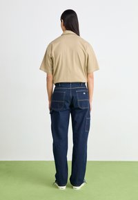 Bežna kratka majica z mehkimi dodatki, v paru s temno modrimi jeans hlačami, ki imajo vidno šivanje in več žepov.