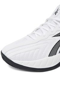 Valge sportlik jalanõu tekstuurse pealiskihi ja musta triibuga. Omaduseks on ümar nina ja must kummist välistald, mis tagab haarduvuse.