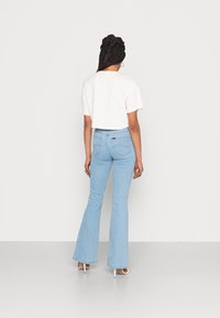 Světle růžové zkrácené tričko a světle modré zvonové džíny s zadními kapsami, obuté s bílými vysokými podpatky. Jednoduchý design, měkká tkanina.