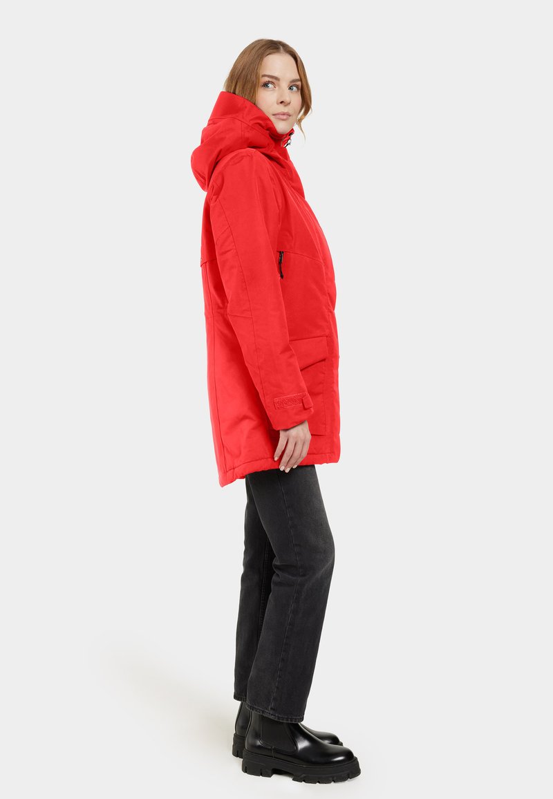 Parka roja con capucha hecha de un material duradero, que cuenta con bolsillos laterales y un bolsillo con cremallera, combinada con unos vaqueros negros de pierna recta y botas.