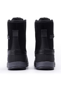 Botas negras con una textura suave, que cuentan con un interior acolchado, suela de goma, acentos de cuero y una tira para facilitar el uso.