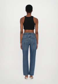 Un haut court noir associé à un jean droit taille haute bleu, mettant en avant cinq poches et une texture en denim classique.