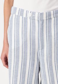 Pantalons en lin rayés avec des rayures verticales bleues et blanches, une fermeture à bouton et une coupe décontractée, mettant en avant un tissu texturé.