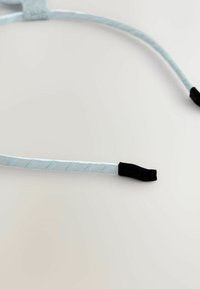Lysblå bånd med fletstruktur, der har sorte gummifor ender. Materialet virker glat og blødt, velegnet til justerbart brug.