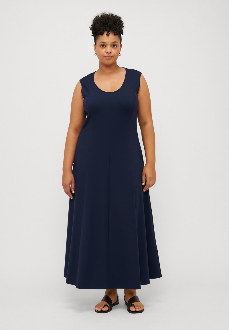 Mörkblå ärmlös maxiklänning i mjukt tyg, med rund halsringning, utsvängd silhuett och sömlös design. Bärs med svarta sandaler.