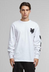 White long-sleeve T-shirt with black spray-painted heart design on the left chest and additional black patterns on the sleeves.